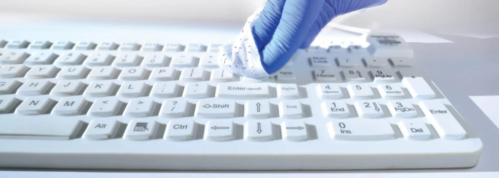 Gloved hand wiping a white MMI Sealed keyboard